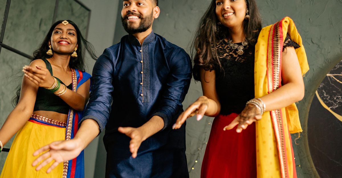 A joyful group of adults dancing in colorful traditional garments, exuding happiness indoors.